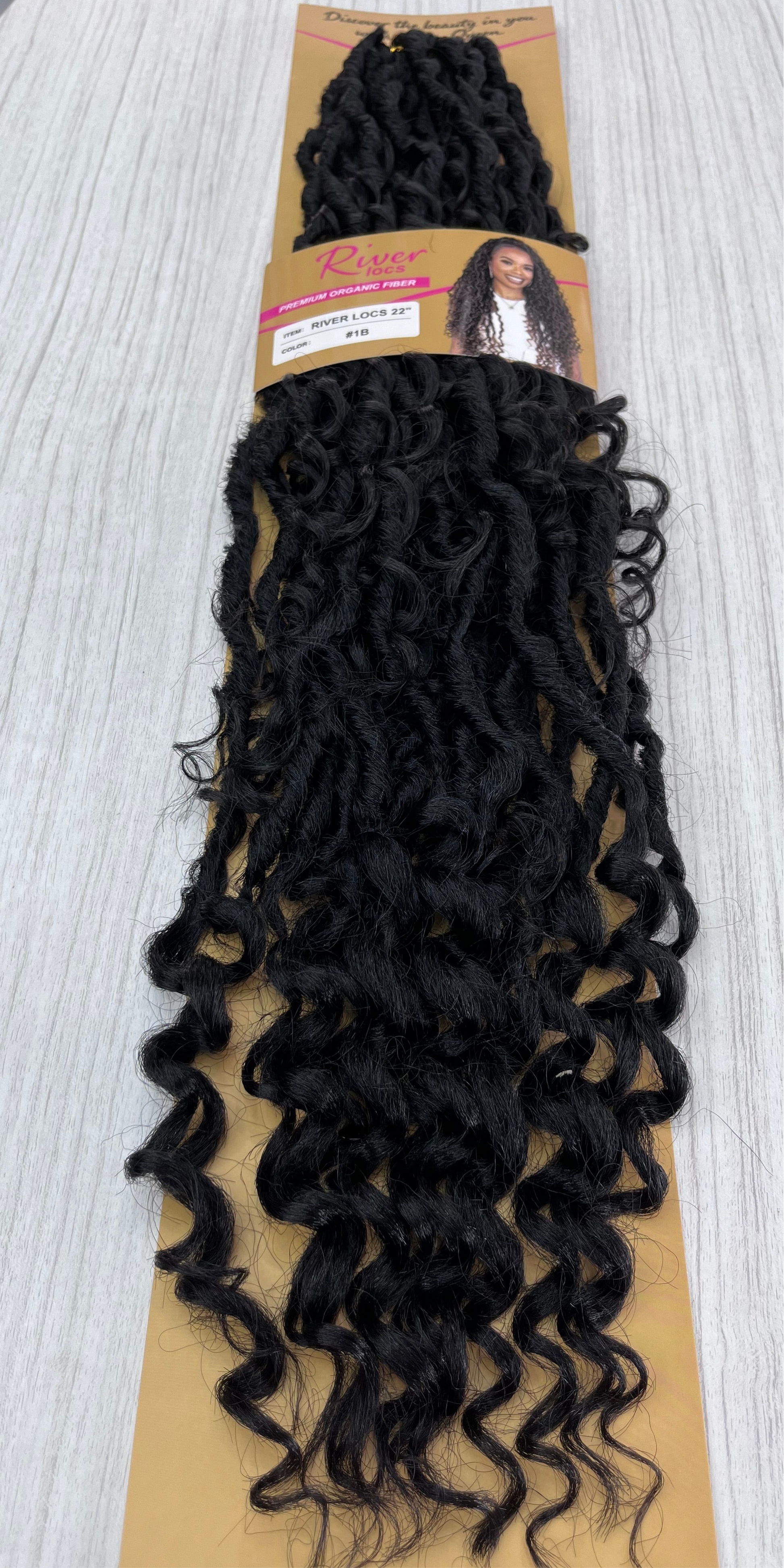 22-inch River Locs crochet hair in #1B off black color with curly ends, packaged and laid on a light wooden background